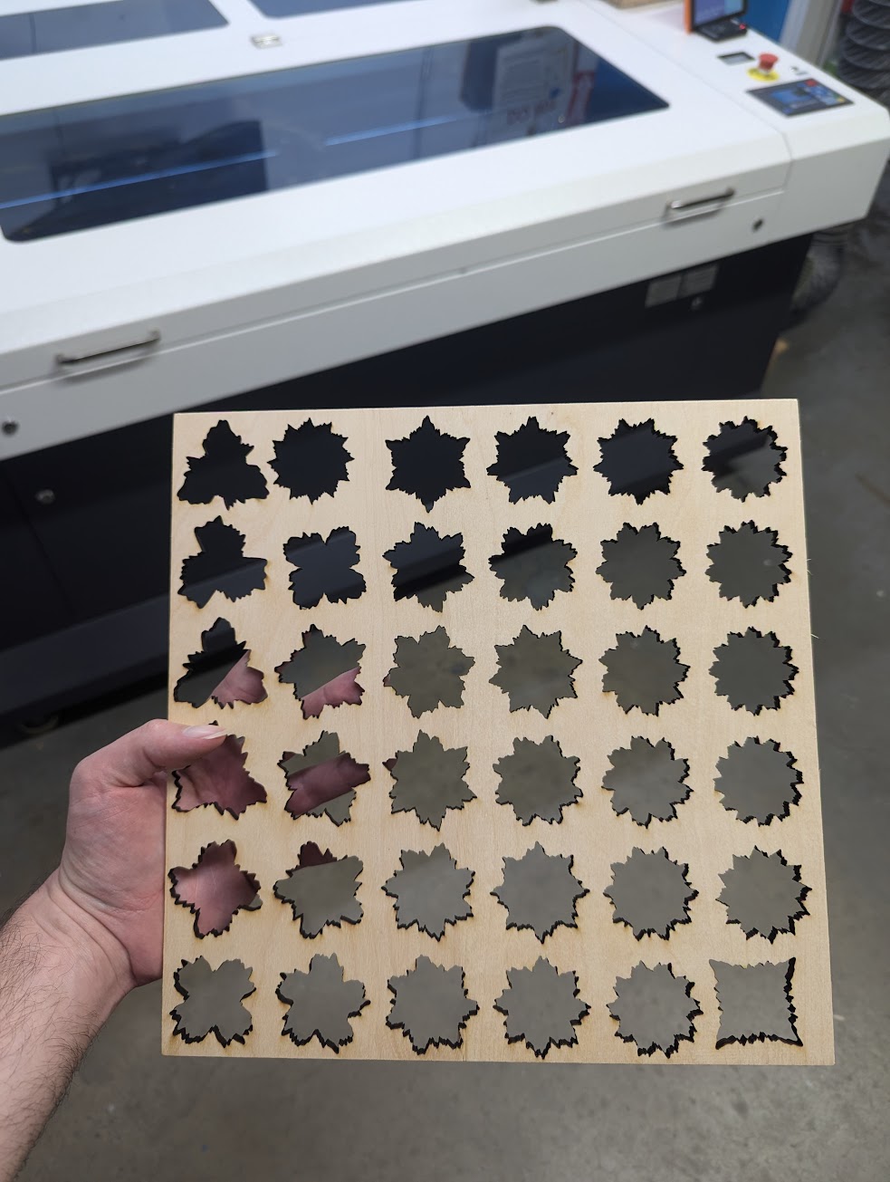 wooden square with jagged symmetrical shapes cut out, with laser cutter visible in background